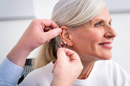 Ältere Frau bekommt ein modernes Hörgerät angepasst, Hörakustik und Hörhilfe-Beratung.